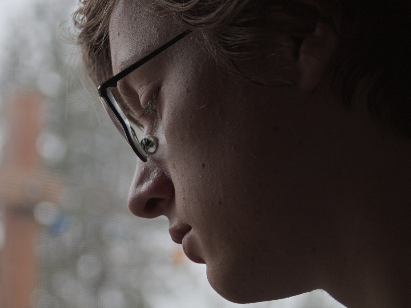 A closeup self-portrait of the photographer from the side with soft rim lighting illumiating a fair toned face with brown wavy hair and black rectangular glasses.